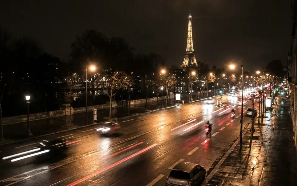 Paris at night from an elevated traffic-camera viewpoint, a wide boulevard with car and scooter headlights